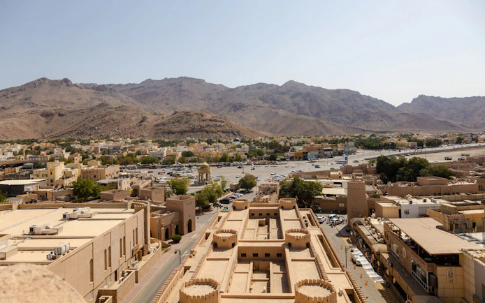 Aerial view of Nizwa Fort with surrounding cityscape and mountains in Oman.