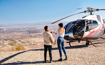 Couple toasting near helicopter with Las Vegas skyline and Red Rock Canyon in background.