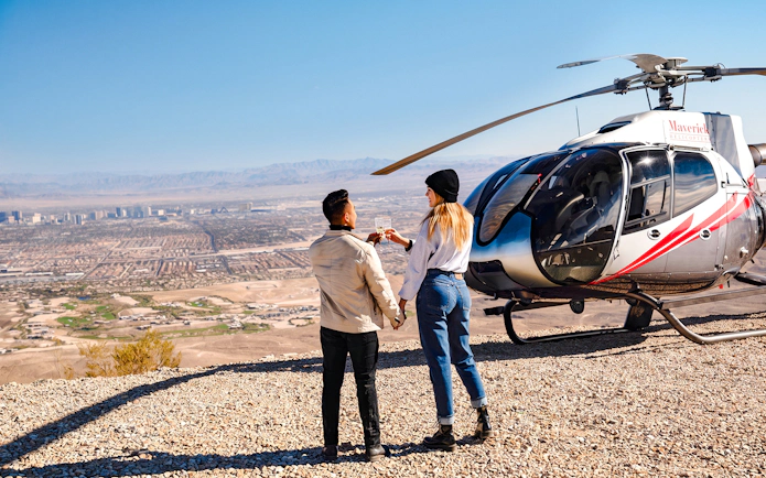 Couple toasting near helicopter with Las Vegas skyline and Red Rock Canyon in background.