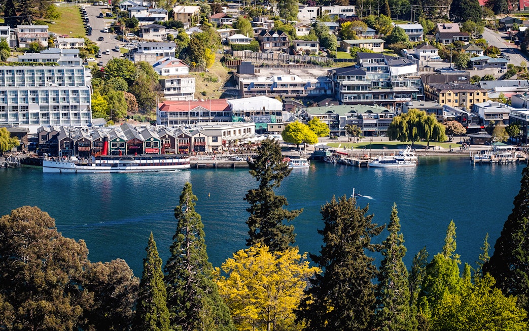 Queenstown waterfront with boats on Lake Wakatipu, surrounded by buildings and trees.