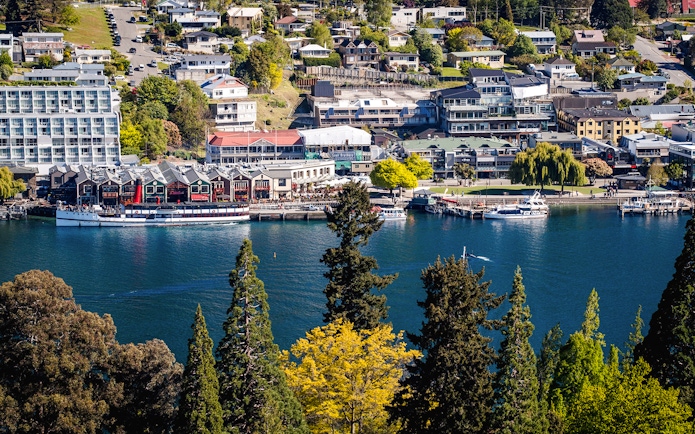 Queenstown waterfront with boats on Lake Wakatipu, surrounded by buildings and trees.