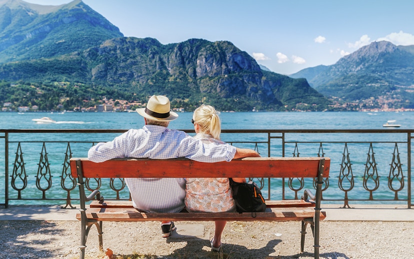 Couple sitting on a bench by Lake Como in Bellagio, Italy, with mountains in the background.