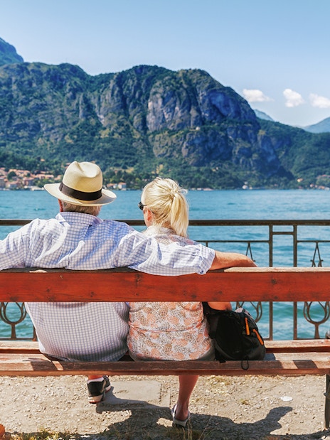 Couple sitting on a bench by Lake Como in Bellagio, Italy, with mountains in the background.