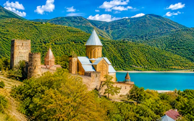 Gergeti Trinity Church in Kazbegi, Georgia, with lush mountains and a blue lake.