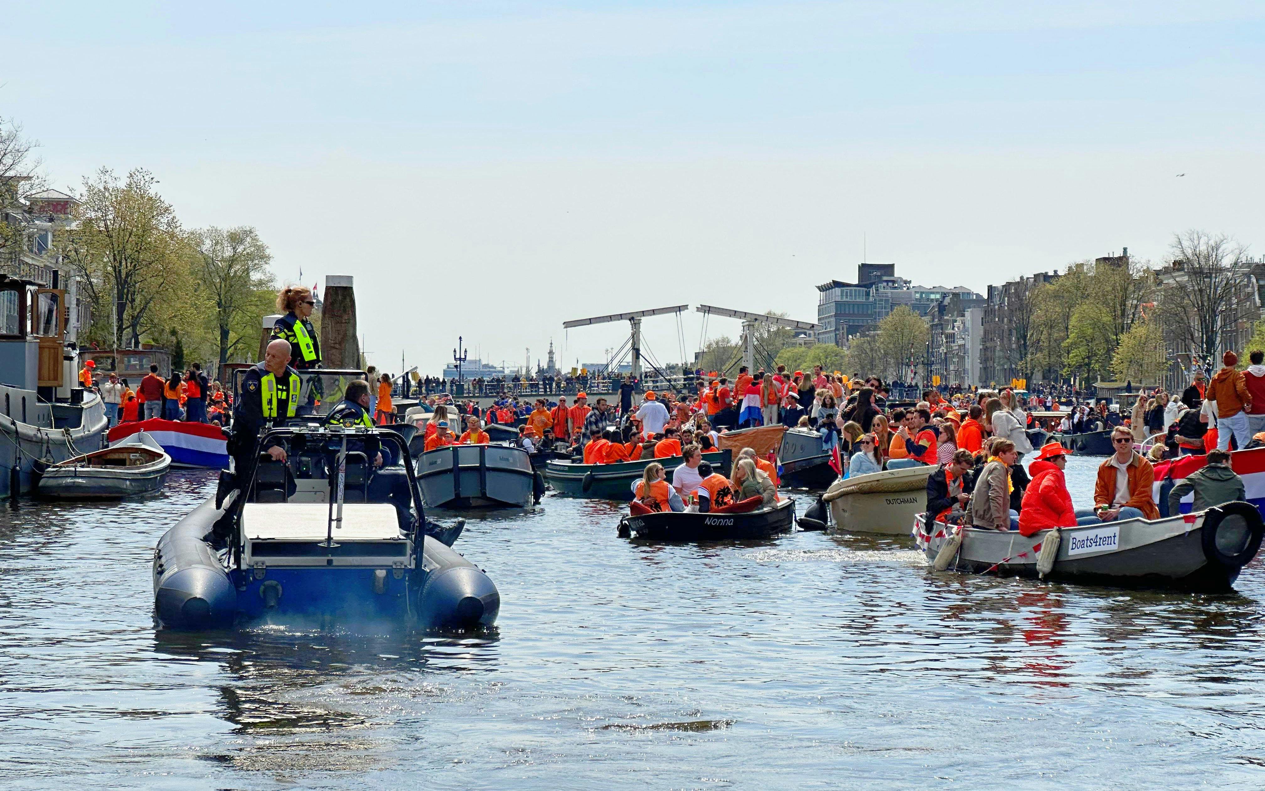 Boats filled with people in orange celebrating Kingsday on Amsterdam canal.