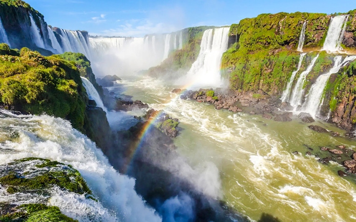 Waterfalls at Iguazu National Park, Argentina, with lush greenery and a visible rainbow.