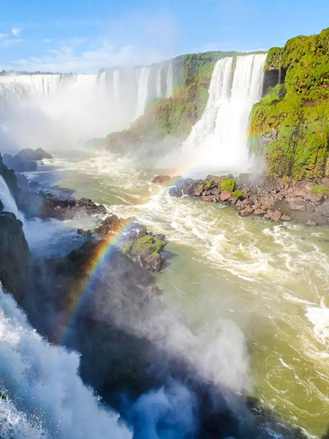 Waterfalls at Iguazu National Park, Argentina, with lush greenery and a visible rainbow.