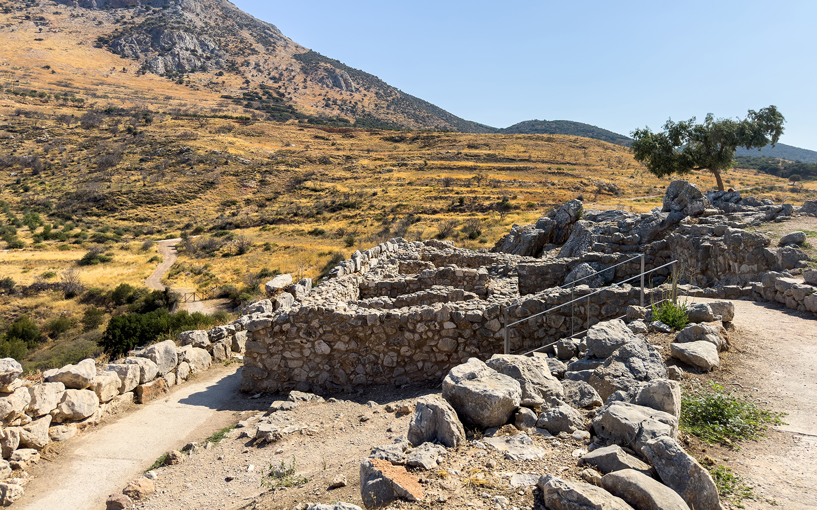 Ancient stone ruins at the archaeological site of Mycenae, Greece, with a mountainous backdrop.