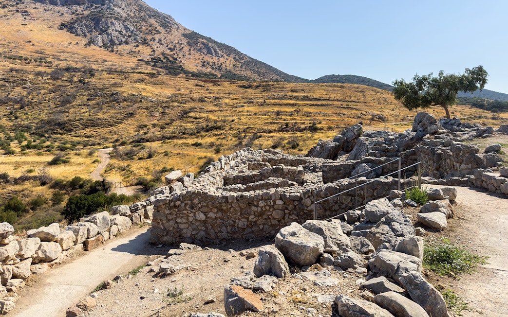 Ancient stone ruins at the archaeological site of Mycenae, Greece, with a mountainous backdrop.