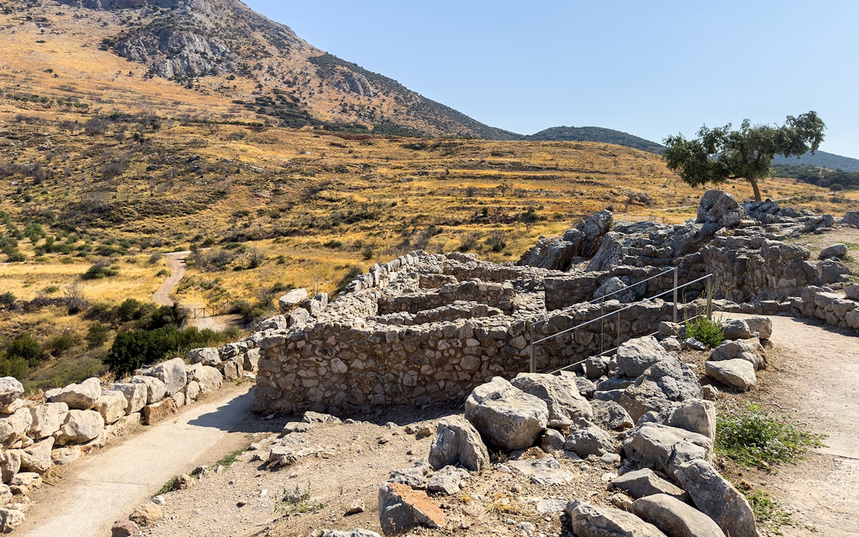 Ancient stone ruins at the archaeological site of Mycenae, Greece, with a mountainous backdrop.