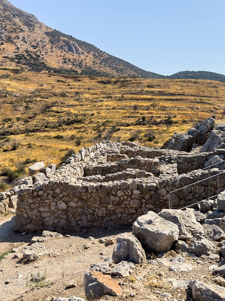 Ancient stone ruins at the archaeological site of Mycenae, Greece, with a mountainous backdrop.