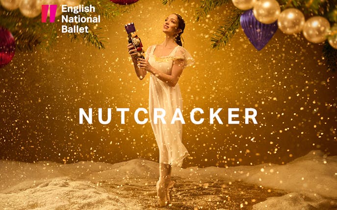 Ballerina holding a nutcracker on stage with festive decorations.