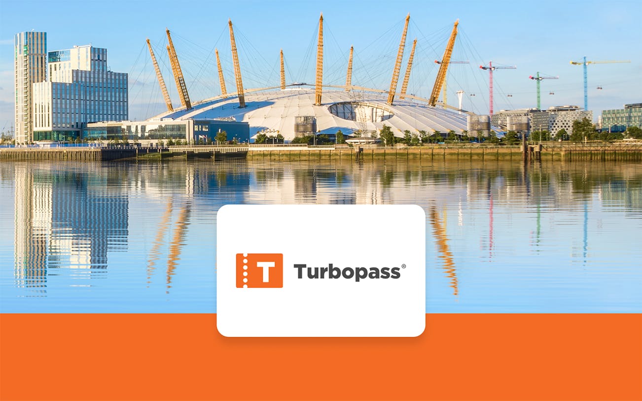 The O2 Arena in London with surrounding buildings and cranes reflected in the Thames River.