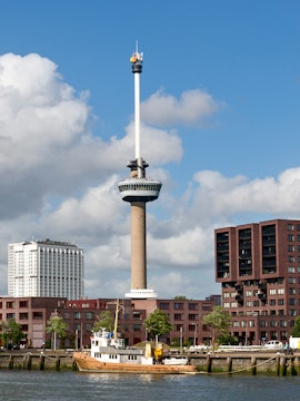 Euromast tower in Rotterdam with surrounding buildings and a boat on the river.