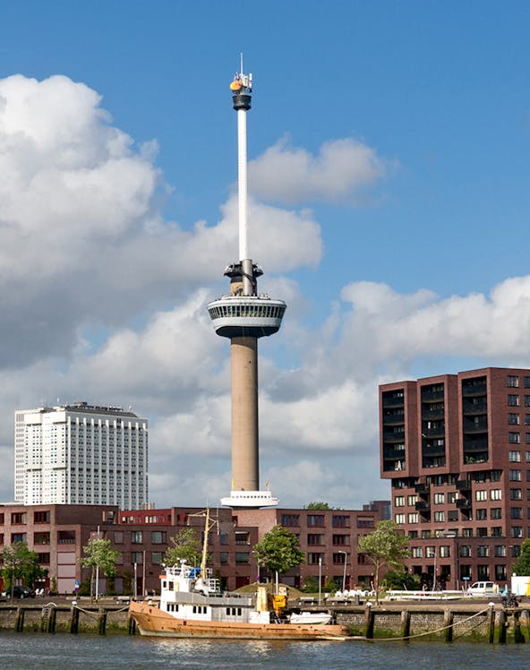 Euromast tower in Rotterdam with surrounding buildings and a boat on the river.