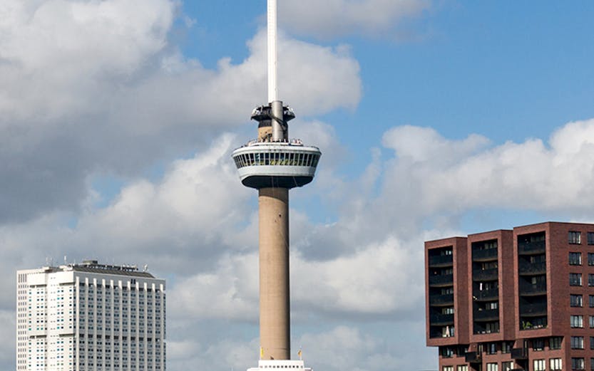 Euromast tower in Rotterdam with surrounding buildings and a boat on the river.