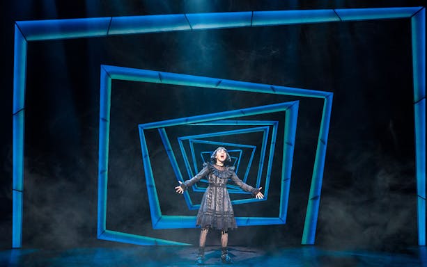 Performer on stage during Beetlejuice West End show with geometric blue backdrop.