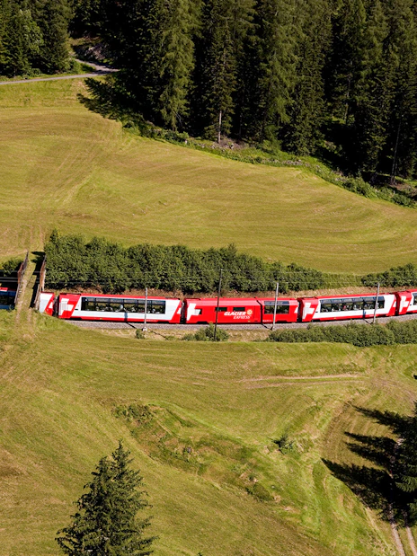 Glacier Express train traveling through lush Swiss countryside with Interrail Pass.