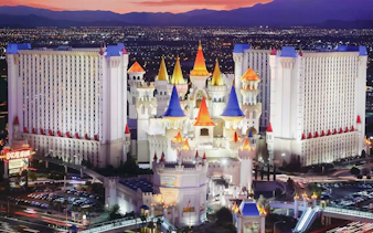 Excalibur Hotel and Casino illuminated at night, Las Vegas skyline in the background.