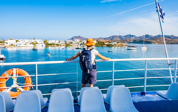 Traveler on ferry viewing Mykonos coastline with white buildings and boats.