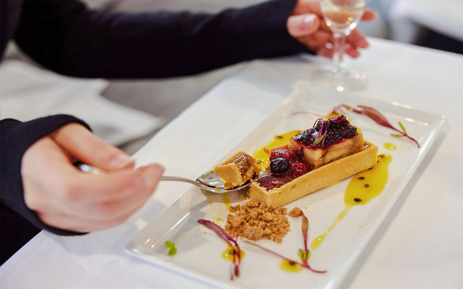 Foie gras terrine with fruit and caviar on a white plate, hand holding a fork.