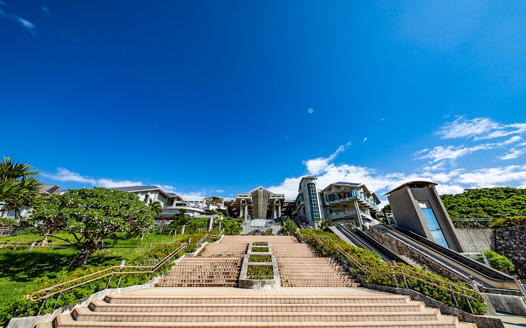 Churaumi Aquarium entrance with stairs and escalators under a clear blue sky.