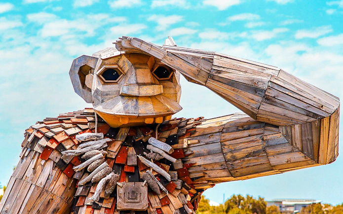 Wooden giant sculpture with hand raised, part of Giant & Dolphin Sightseeing Cruise.
