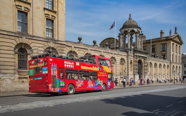 Red double-decker bus on Oxford street near historic building, part of Oxford by Rail day tour from London.