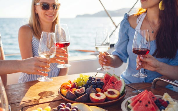 People enjoying wine and fresh fruit on a boat with ocean view.