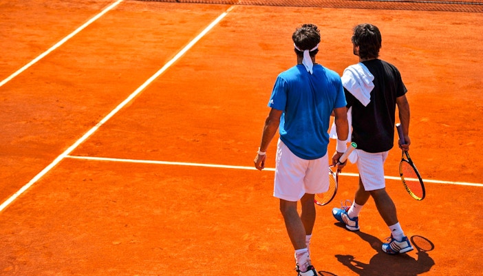 Tennis players walking on clay court at Roland-Garros Stadium.