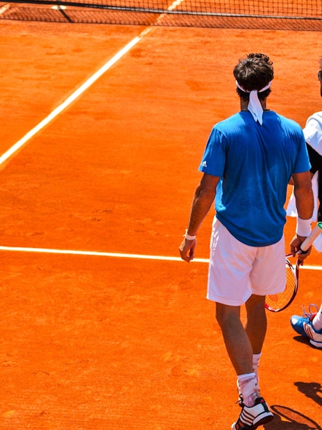 Tennis players walking on clay court at Roland-Garros Stadium.