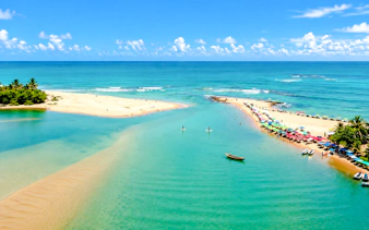 Beach and river meeting at Caraíva, Porto Seguro, with colorful umbrellas and boats.