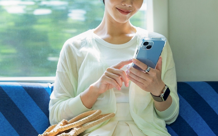 Woman on train using cellphone, seated by window with woven bag.