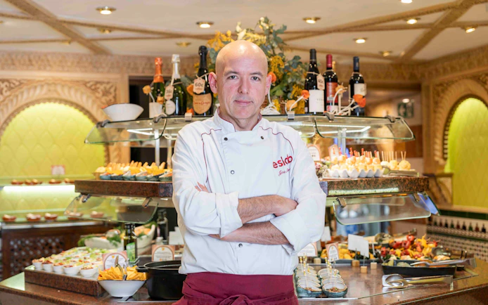 Chef at Tablao Cordobes standing in front of a tapas display in Barcelona.