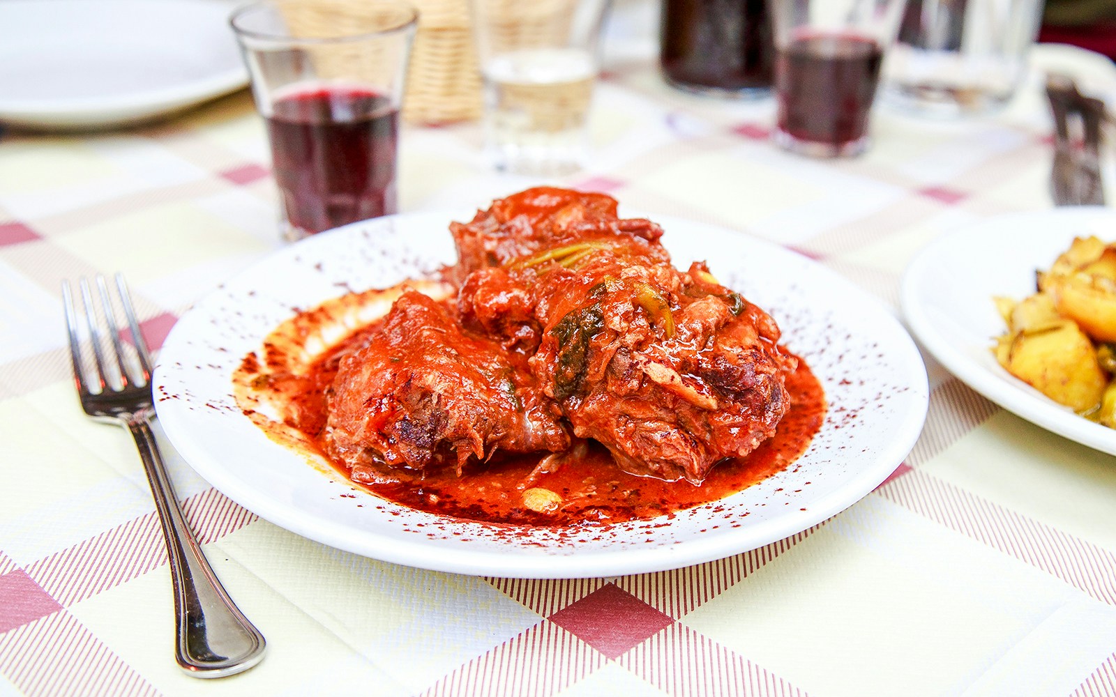 Coda alla vaccinara dish served with red wine on a checkered tablecloth.
