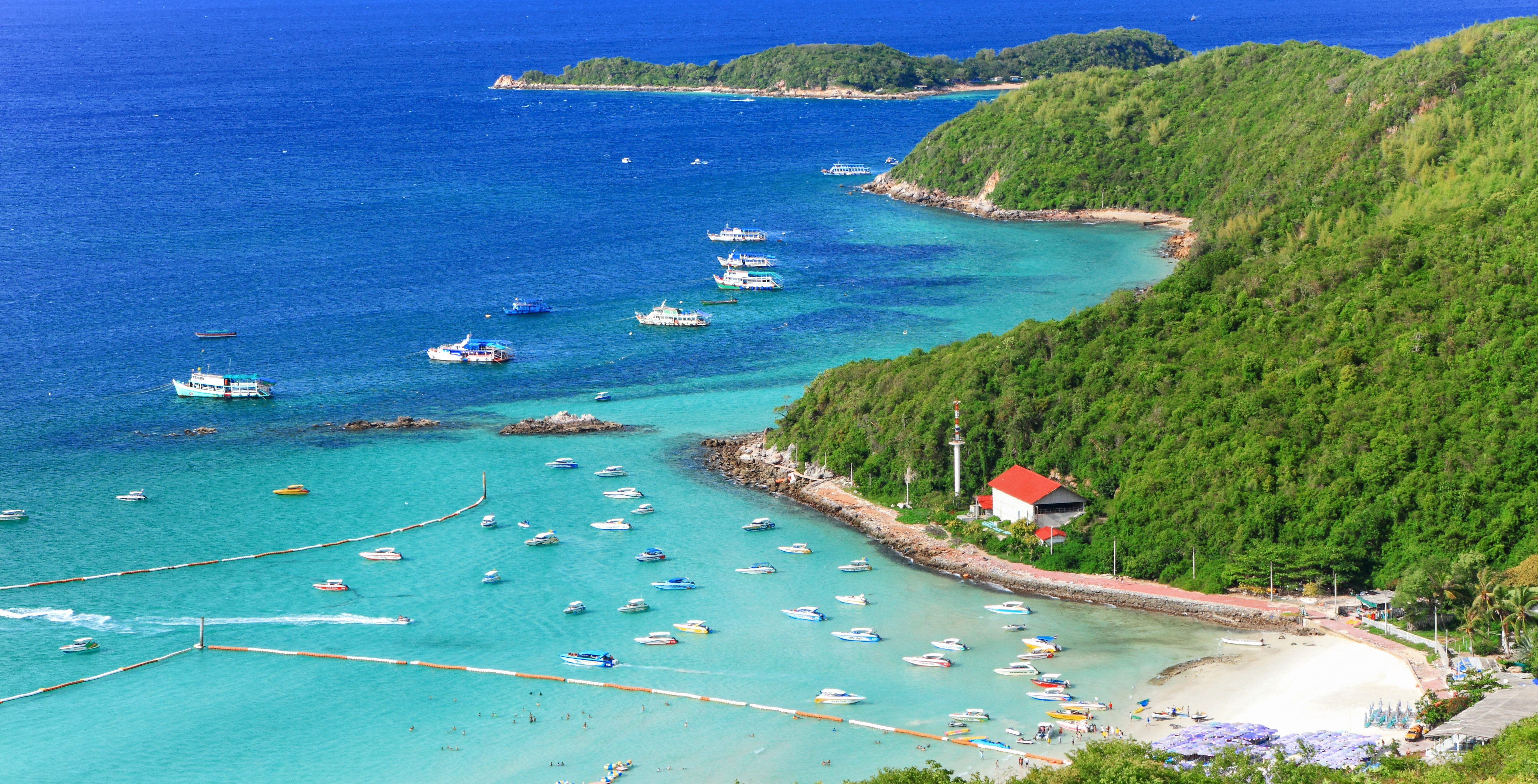 Tourists enjoying a sunny day on the sandy beach of Koh Larn Island, Pattaya, with clear blue waters.