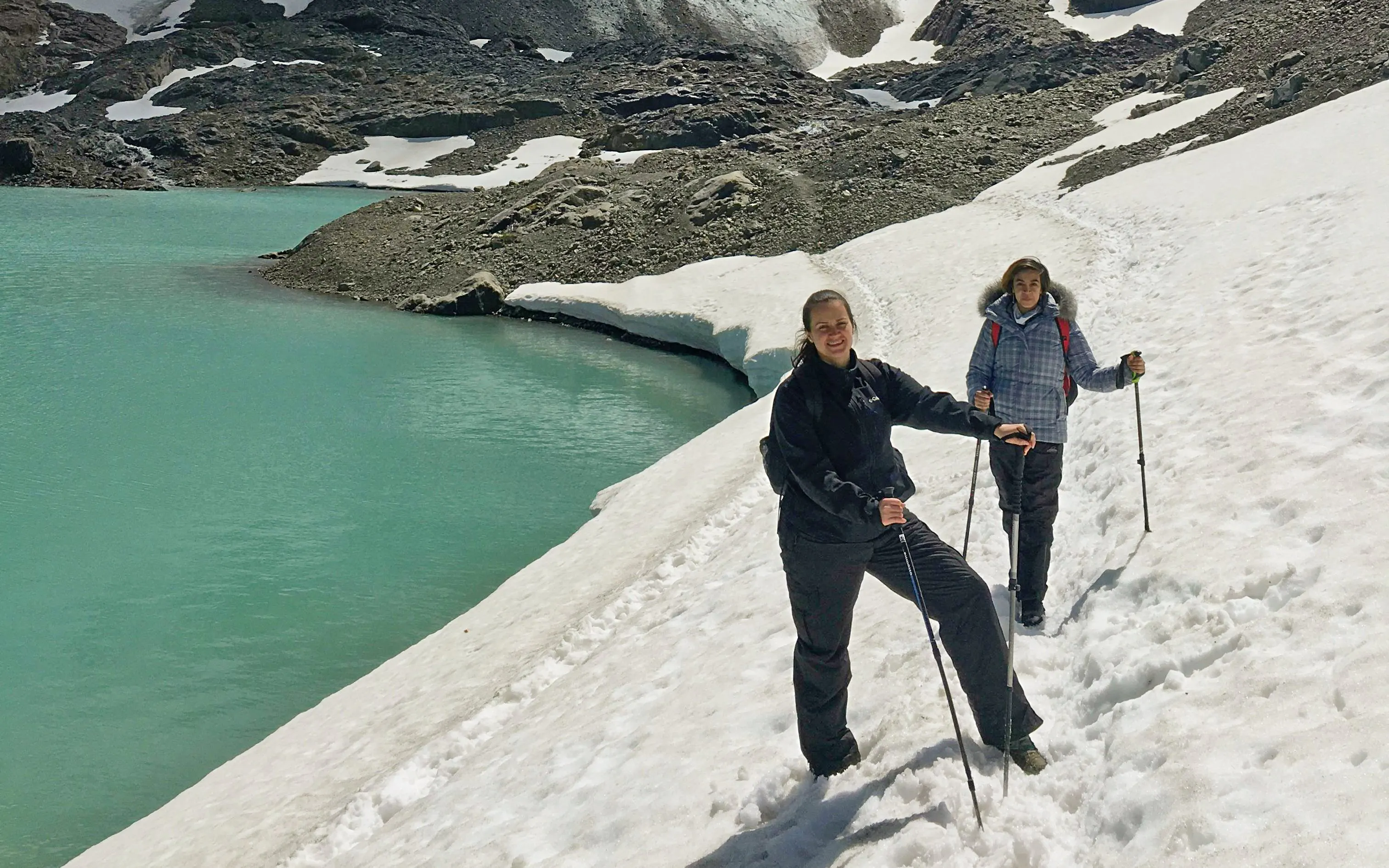 Hikers on snowy trail by turquoise Laguna de los Témpanos, Vinciguerra Glacier.
