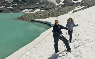 Hikers on snowy trail by turquoise Laguna de los Témpanos, Vinciguerra Glacier.