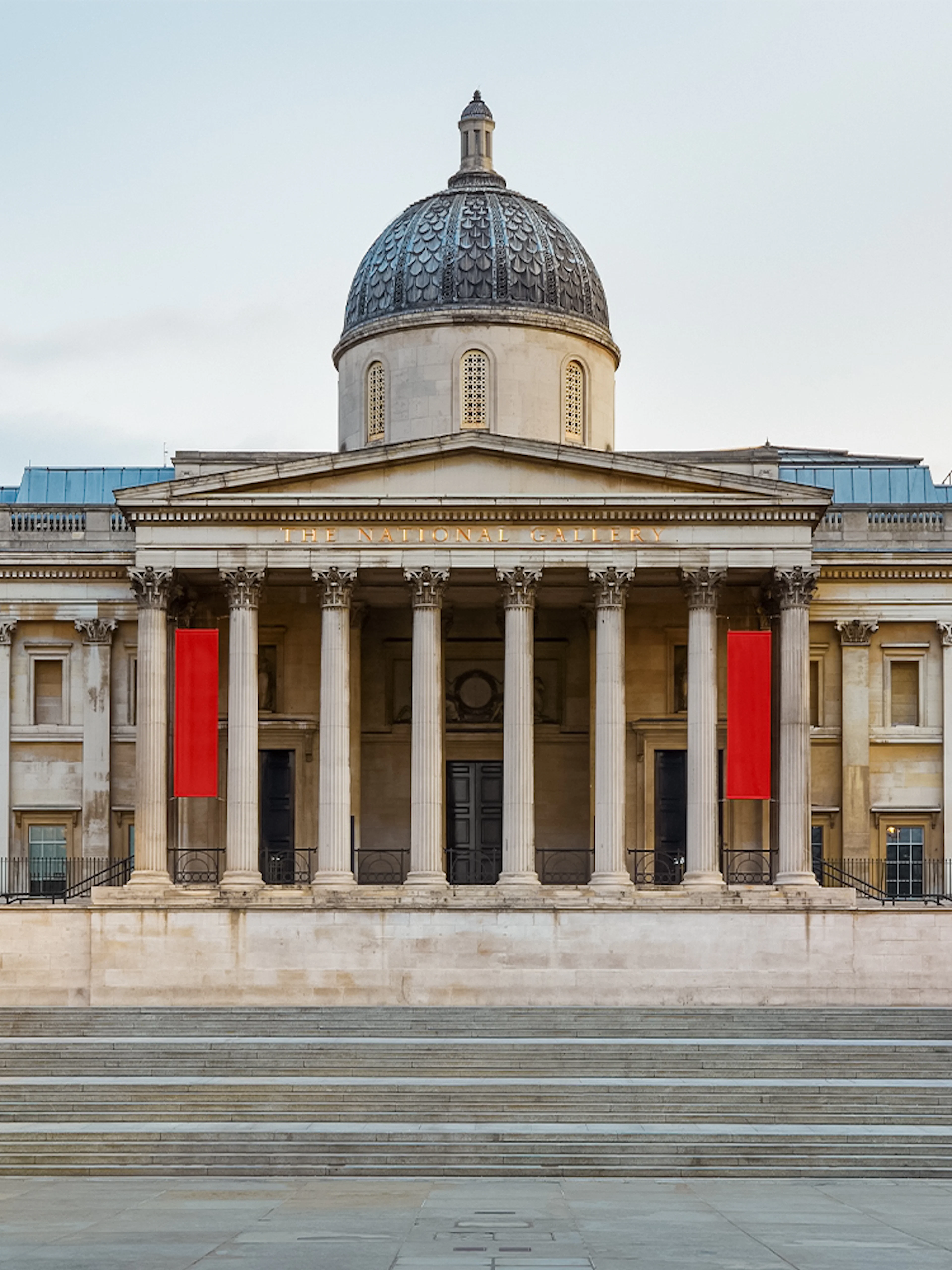 National Gallery London facade with steps and lampposts in Trafalgar Square, UK.