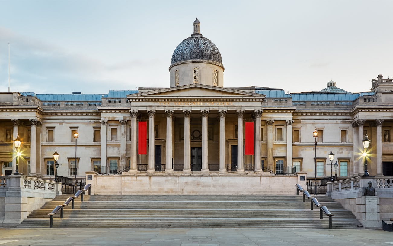 National Gallery London facade with steps and lampposts in Trafalgar Square, UK.
