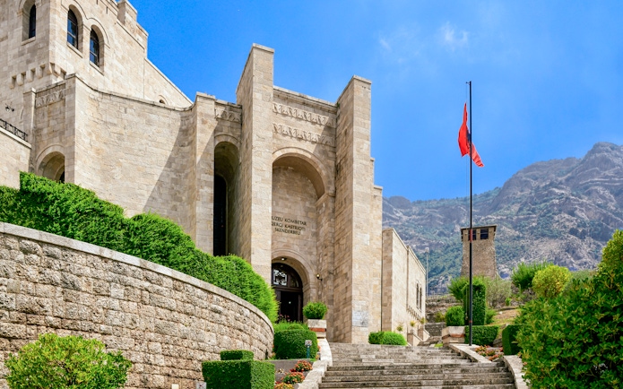 Skanderbeg Museum entrance at Kruje Castle, Albania, with Albanian flag and mountain backdrop.