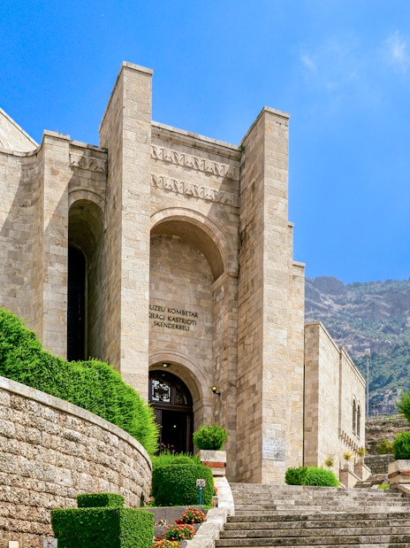 Skanderbeg Museum entrance at Kruje Castle, Albania, with Albanian flag and mountain backdrop.