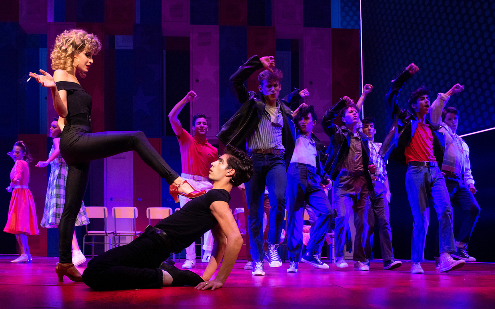 Cast performing a dance scene from the musical Grease on stage.