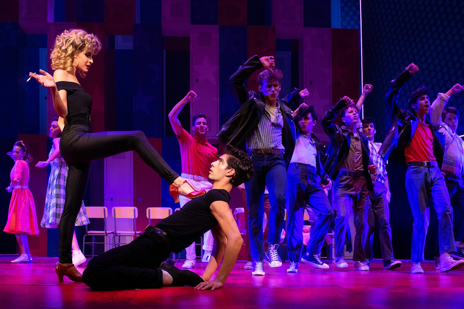 Cast performing a dance scene from the musical Grease on stage.