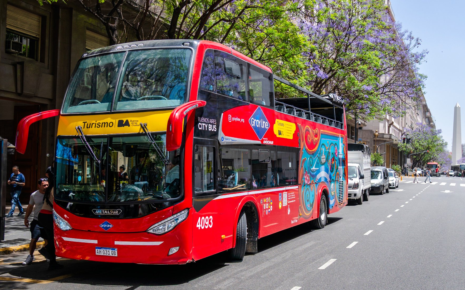 Hop-on hop-off bus near Obelisco de Buenos Aires on a tree-lined street.