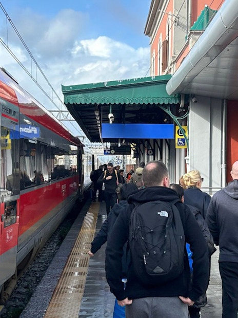Passengers walking along a platform beside a red train at a station.