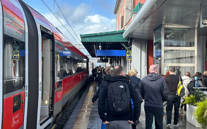 Passengers walking along a platform beside a red train at a station.