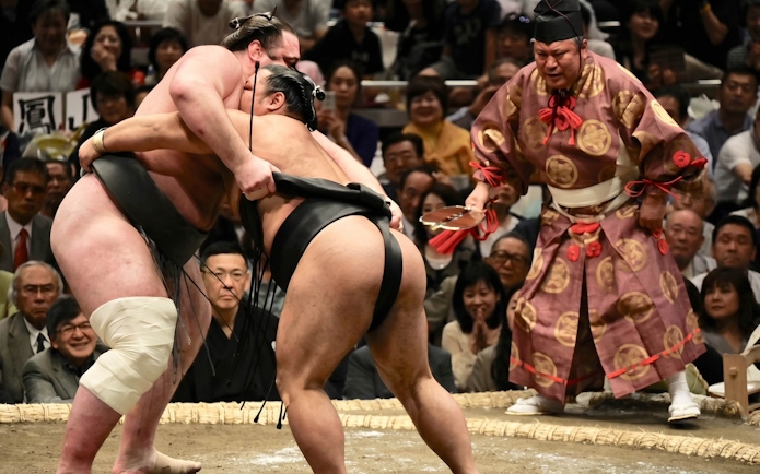 Sumo wrestlers competing in Tokyo Grand Sumo Tournament with referee observing.