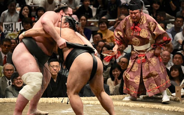 Sumo wrestlers competing in Tokyo Grand Sumo Tournament with referee observing.