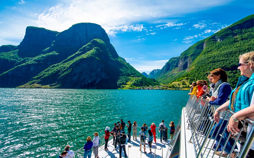 Tourists on a cruise ship deck enjoying views of Nærøyfjord's mountains and water.
